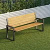 A modern outdoor bench made of wood and dark metal, placed on a green lawn in front of a white slatted fence and greenery. Anteprima dell’immagine prodotto