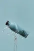 A blue water bottle is shown with water splashing around it against a light blue background. Produktbild-Vorschau