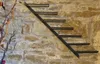 A metal wine rack mounted on a stone wall, with decorative branches to the left. Podgląd zdjęcia produktu