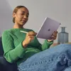 A woman is sitting on a couch, holding a purple iPad and using a stylus. Podgląd zdjęcia produktu
