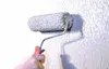 A hand is using a paint roller to apply a textured, light gray putty to a wall. Produktbild-Vorschau