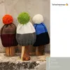 Three knitted hats with pom-poms displayed on wooden stands. Produktbild-Vorschau