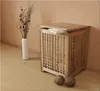 A wooden laundry hamper with a lid, a white vase with dried flowers, and two woven balls on a carpeted floor, next to a wall. Náhled obrázku produktu