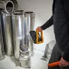 A person is holding a portable work light near a stack of metal pipes. Produktbild-Vorschau