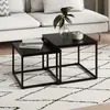 Two black nesting coffee tables are placed on a white rug with a black geometric pattern in a living room setting, with a portion of a light-colored sofa visible in the background. Produktbild-Vorschau