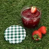 A jar of strawberry jam with a checkered lid and strawberries on grass. Produktbild-Vorschau