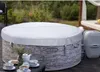 A round hot tub covered with a white lid, situated on a wooden deck outdoors. Produktbild-Vorschau