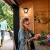 A woman is arranging flowers on a table, with a man and a dog in the background. Anteprima dell’immagine prodotto