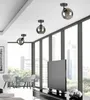 A modern living room with large windows overlooking a city skyline, featuring three black ceiling lights. Produktbild-Vorschau