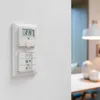 A white wall-mounted thermostat with a digital display and control buttons. Produktbild-Vorschau