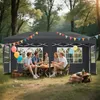 A group of people are sitting around a table under a gray canopy tent in a wooded area. Náhled obrázku produktu