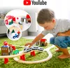 A young boy is playing with a wooden train set on a green carpet. The train set includes tracks, buildings, a train, and accessories. The image also features a YouTube logo and inset images of other parts of the train set. Náhled obrázku produktu
