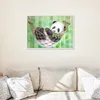 A framed painting of a panda in a hammock is displayed on a wall above a sofa. Náhled obrázku produktu