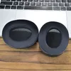 Two black ear pads are placed on a wooden surface in front of a laptop keyboard. Produktbild-Vorschau