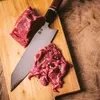 A piece of raw meat and sliced meat are on a wooden cutting board next to a knife. Podgląd zdjęcia produktu