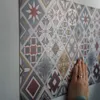 A hand is touching a wall covered in patterned vinyl stickers. Produktbild-Vorschau