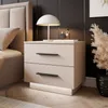 A bedside table with two drawers next to a bed, featuring a lamp and decorative items. Produktbild-Vorschau