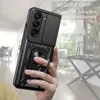 A hand holding a black phone case with a ring holder, with a blurred background of an indoor setting. Produktbild-Vorschau