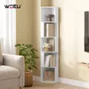 A white corner shelf unit filled with books and decorative items, placed next to a sofa and a potted plant in a living room setting. Produktbild-Vorschau