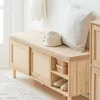 A wooden shoe bench with storage, featuring a cushion, a hat, and a pillow, placed in a hallway or entryway. Produktbild-Vorschau