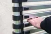 A person's hand is shown adjusting a section of a telescopic ladder. Produktbild-Vorschau