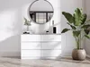 A white dresser with six drawers is shown in a well-lit room with a large round mirror above it and a potted plant to the right. Produktbild-Vorschau
