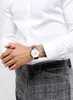 A man wearing a white dress shirt and checkered trousers, showing off his watch. Produktbild-Vorschau