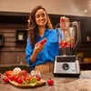 A woman is preparing ingredients for a blender in a kitchen. Produktbild-Vorschau