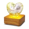 A heart-shaped glass lamp with a firework effect, resting on a wooden base. Produktbild-Vorschau