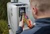 A person is working on an outdoor air conditioning unit, using electrical testing tools. Náhľad obrázku produktu