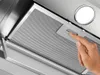 A close-up view of a person's hand interacting with a metal mesh filter inside a kitchen range hood. Voir les images du produit
