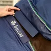 A close-up of a blue horse blanket with a hand adjusting a velcro strap. The Bucas logo is visible on the strap. Produktbild-Vorschau