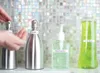 A hand is pressing a pump dispenser on a silver bottle, with other bottles of lotion, hand sanitizer, and dish soap visible. Produktbild-Vorschau