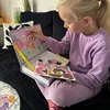 A young girl is playing with a magnetic puzzle book on a couch. Produktbild-Vorschau