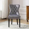 A gray velvet dining chair with nailhead trim and black legs is shown in a room with curtains and a wooden cabinet. Náhled obrázku produktu