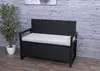 A black poly-rattan storage bench with a gray cushion is shown in an outdoor or patio setting. Voir les images du produit