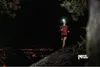 A woman is running on a trail at night with a headlamp on, overlooking a city. Náhled obrázku produktu
