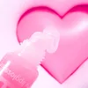 A close-up of a lip gloss tube with the applicator extended, in front of a blurred pink heart. Anteprima dell’immagine prodotto