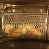 A rotisserie basket filled with vegetables inside an oven. Produktbild-Vorschau