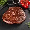 A close-up of a cooked flank steak seasoned with pink salt, with tomatoes and peppercorns in the background. Produktbild-Vorschau