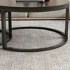 A close-up view of the base of a round coffee table with a metal frame, resting on a textured gray carpet. Náhľad obrázku produktu