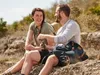 A couple sitting on rocks outdoors, smiling and talking. Podgląd zdjęcia produktu