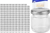 A large group of small glass jars with silver lids are arranged in rows on the left side of the image. On the right side, a single jar with a silver lid is shown, along with a small booklet with text on it. Náhled obrázku produktu