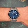 A man's wrist wearing a silver and blue analog watch. Produktbild-Vorschau
