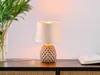 A table lamp with a textured ceramic base and a fabric shade sits on a dark wooden surface next to a vase of plants and a book. Anteprima dell’immagine prodotto