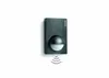 A dark gray motion sensor mounted on a white wall with a subtle graphic indicating wireless transmission. Anteprima dell’immagine prodotto