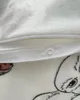 A close-up view of a zipper and a snap closure on a white fabric with a printed pattern of a character. Produktbild-Vorschau