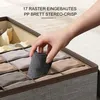 A hand is placing a rolled-up gray sock into a divided storage box. Produktbild-Vorschau