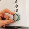 A hand is shown adjusting the dial on a white appliance, likely a toaster, with several control buttons visible above the dial. Voir les images du produit