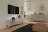 A modern living room with a TV mounted on the wall above a media console. A sideboard with a lamp and decorative items is visible on the right. Produktbild-Vorschau
